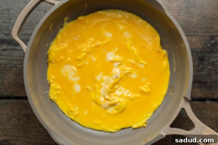 Overhead view of scrambled eggs spread out across a hot skillet to create a Mexican omelette.