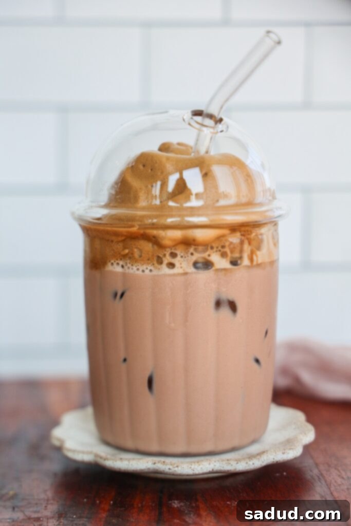Mocha dalgona whipped coffee – a decadent and creamy chocolate coffee drink in a glass with ice, topped with fluffy whipped coffee foam and a sprinkle of cocoa powder.