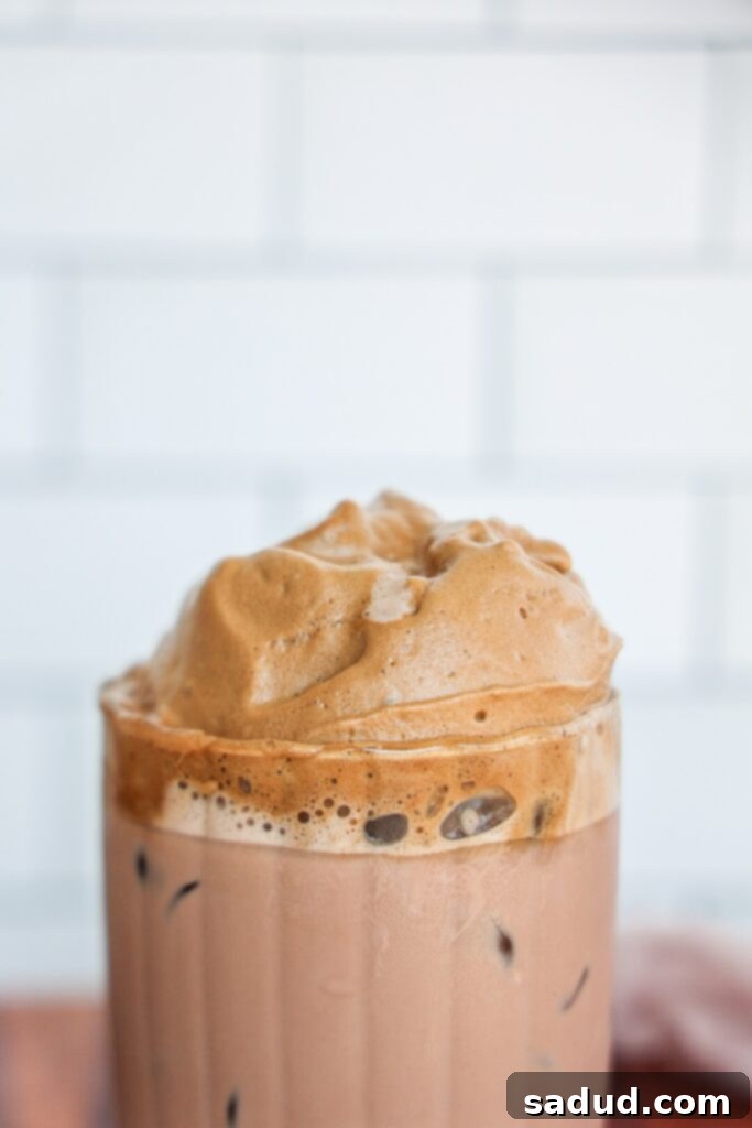 Hand holding a glass of beautifully layered whipped Dalgona Coffee Mocha, ready to drink.