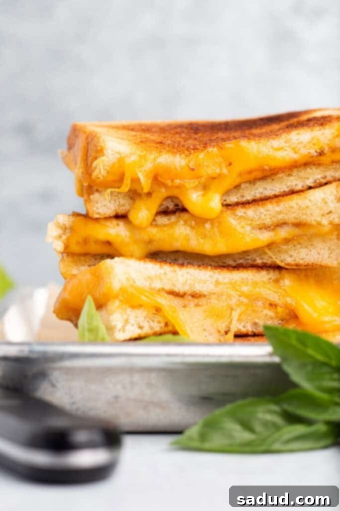 Side view of 4 toasted grilled cheese halves stacked on top of eachother with cheese oozing out toward the camera.