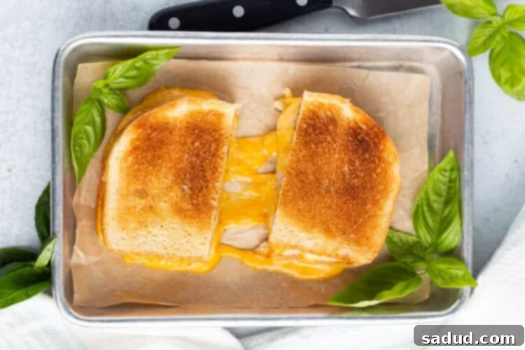 Overhead view of a toasted grilled cheese sandwich on a baking sheet. Sandwich is cut in half to show cheese pull.