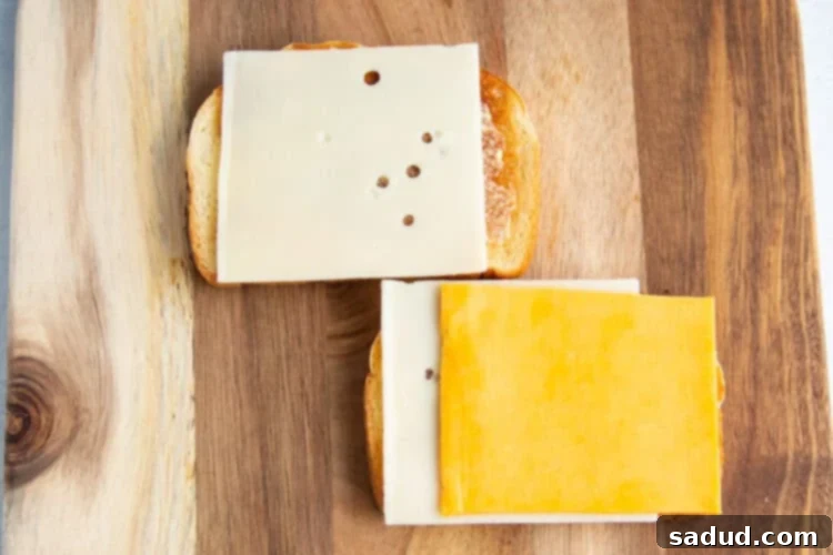 Overhead view of two slices of buttered toast topped with 3 slices of cheese on a wooden cutting board.