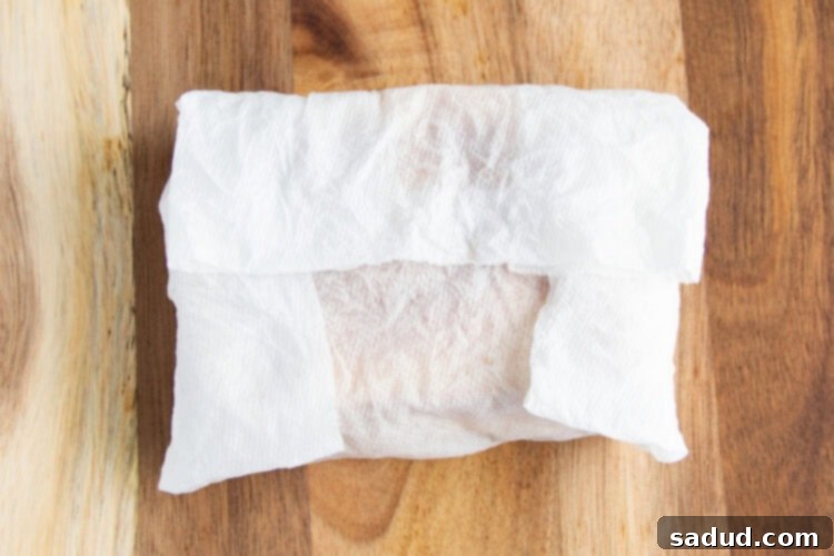 Overhead view of a toasted grilled cheese sandwich wrapped in a damp paper towel on a wooden cutting board.
