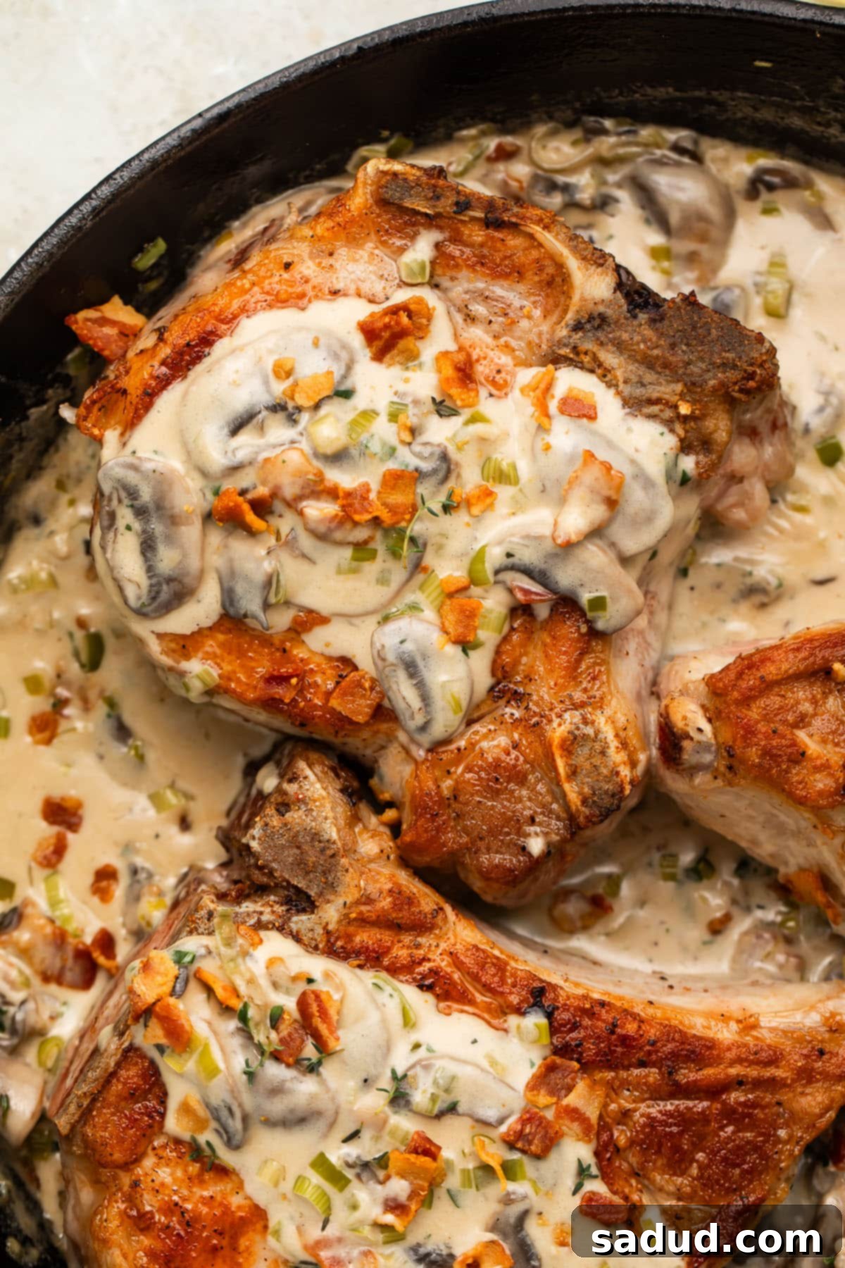 Keto smothered pork chops in a cast iron skillet with a creamy sauce, garnished with fresh herbs.