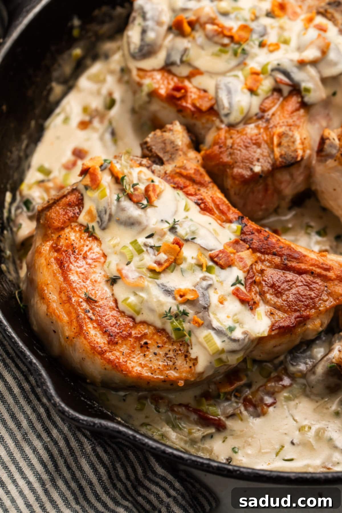 Two keto smothered pork chops on a plate, drenched in creamy mushroom garlic sauce with crispy bacon bits.