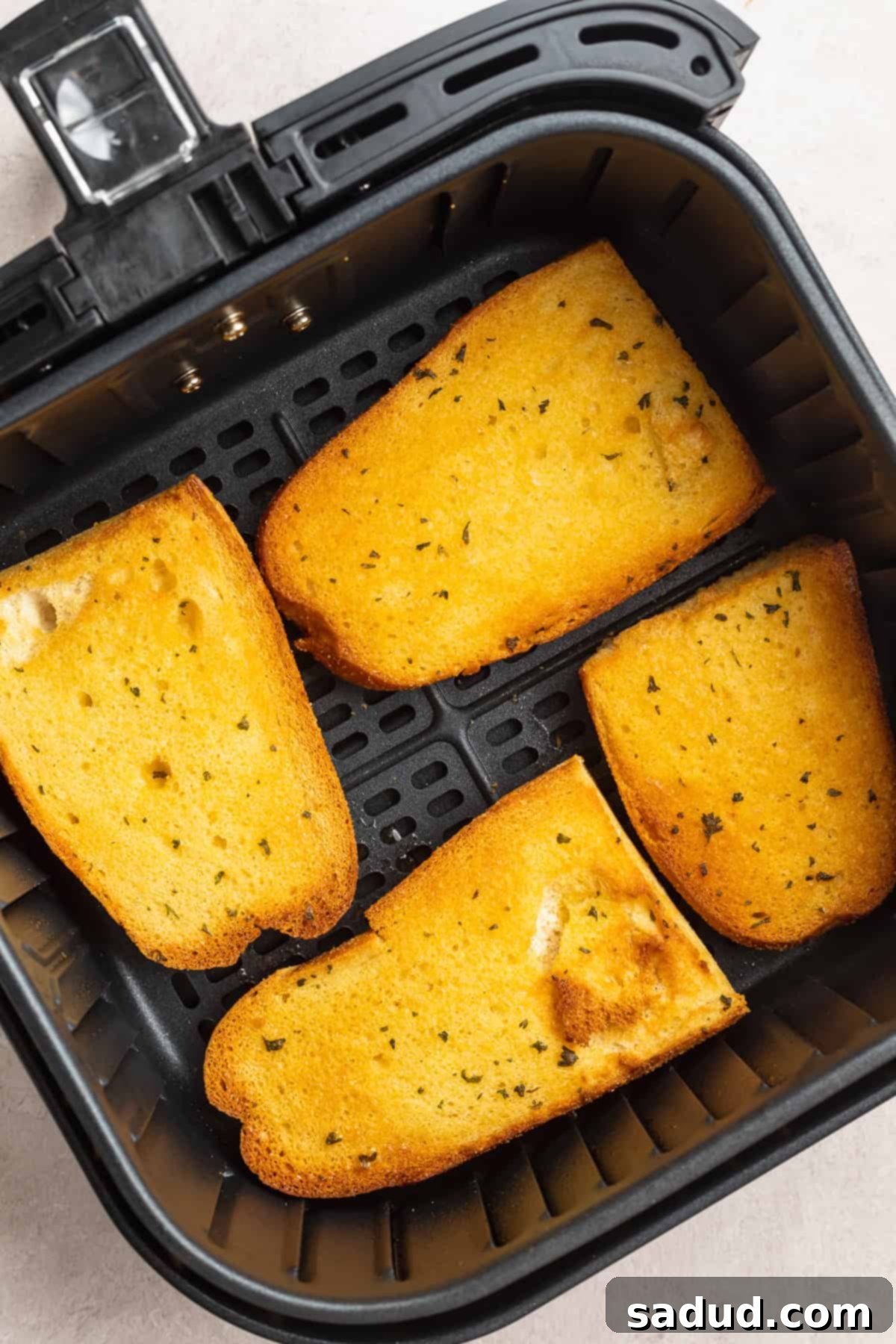 Overhead view of 4 pieces of garlic Texas toast in an air fryer basket on a white countertop.