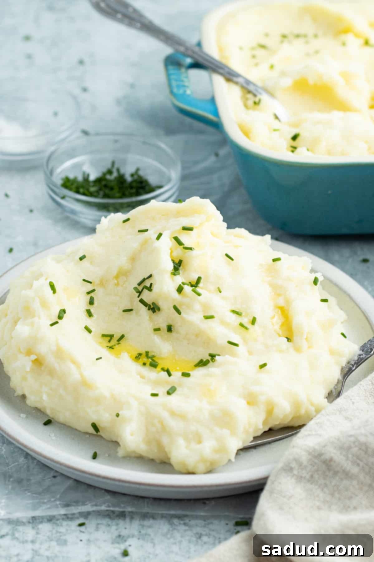 Side view of a bowl of fluffy potato mousseline in front of a casserole dish of potato mousseline, highlighting its smooth texture and rich appearance.