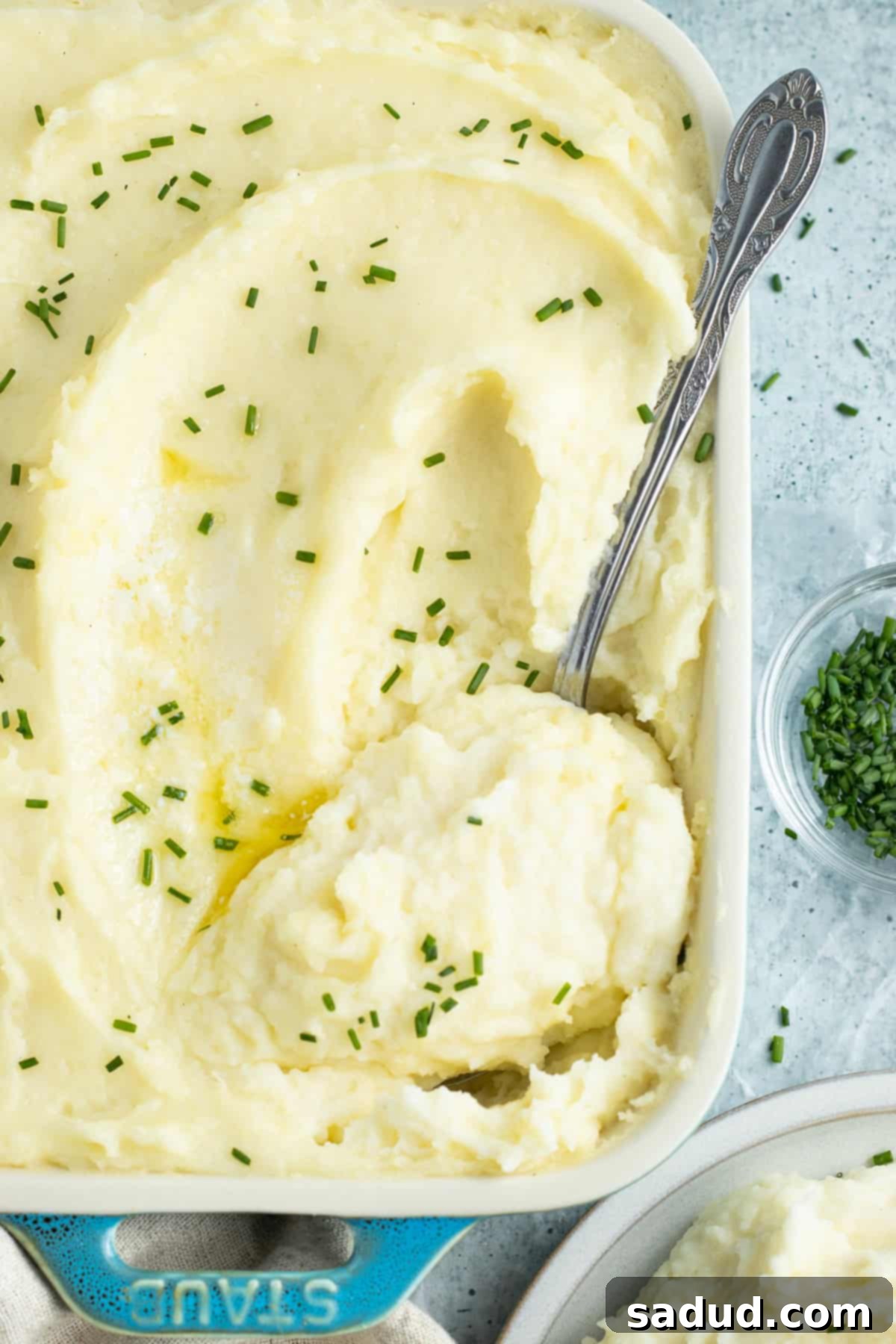 Overhead view of a casserole dish of potato mousseline with a silver spoon scooping potatoes out, showing its creamy texture.