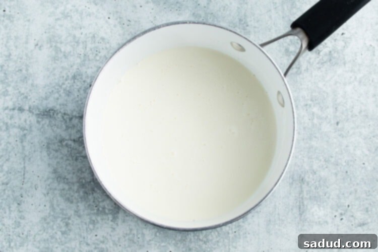Overhead view of milk and cream being gently warmed in a medium saucepan on a white countertop.