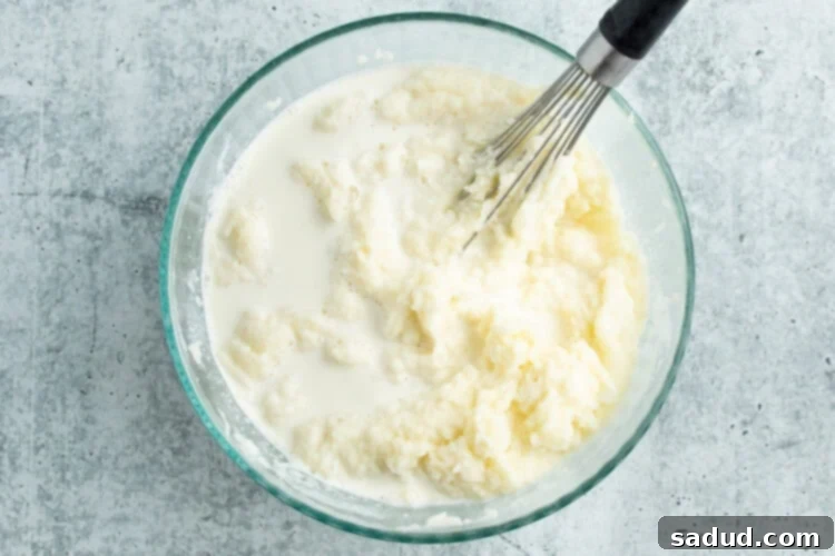 Overhead view of milk and cream added to a bowl of riced potatoes and then whisked until fluffy and smooth.