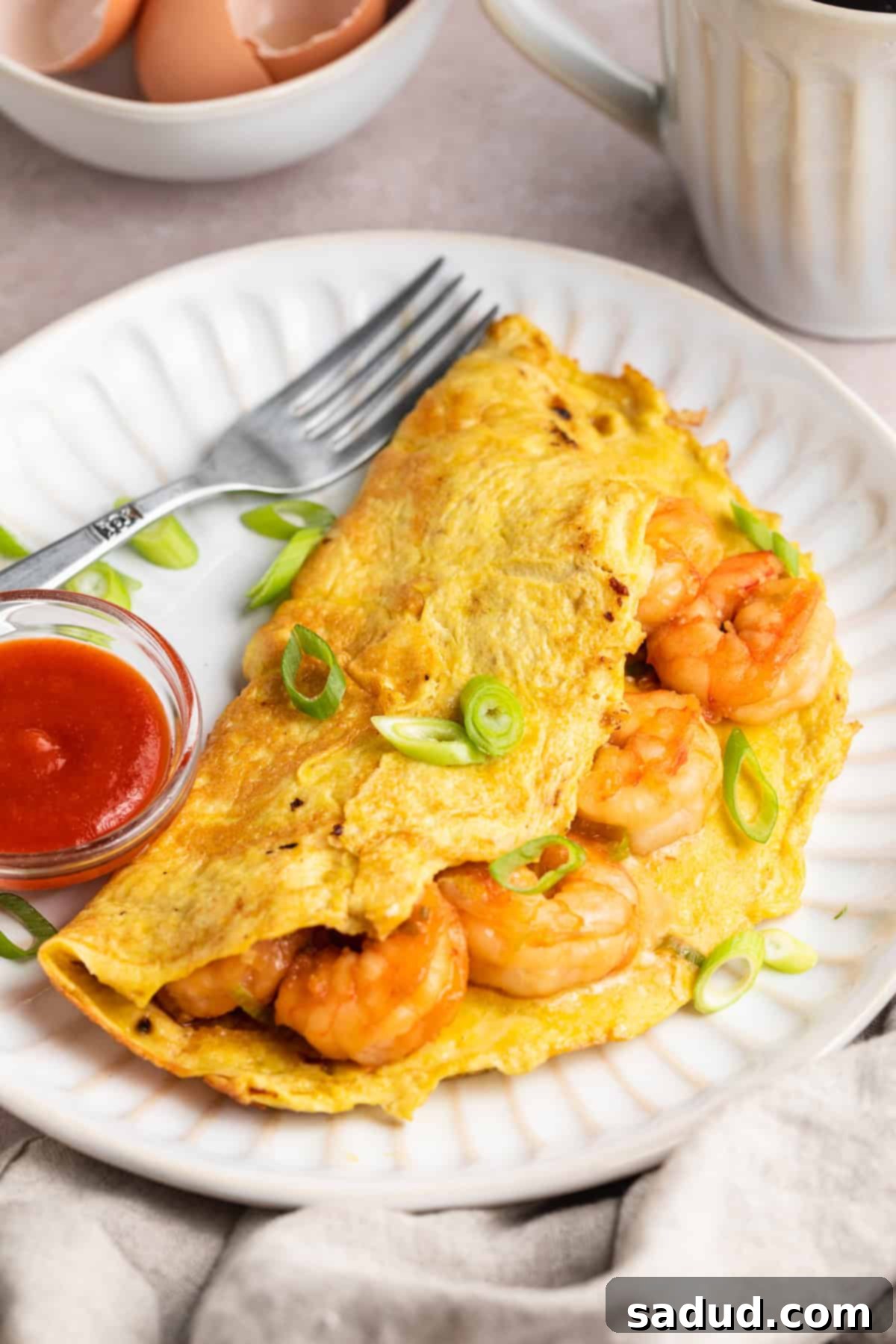 3/4-angle view of a folded omelette stuffed full with tender shrimp on a white plate next to a small bowl of ketchup.