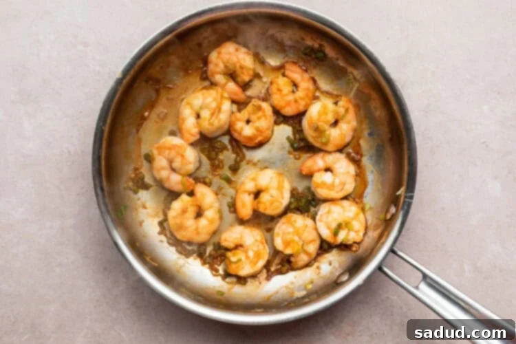 Overhead view of sautéed shrimp and diced green onion in a large silver skillet on a neutral countertop.