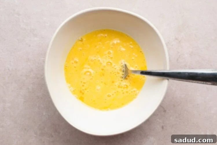 Overhead view of eggs and milk mixed together in a white bowl until egg mixture is pale yellow.
