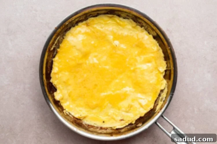 Overhead view of firm, cooked eggs in a large silver skillet on a neutral countertop.