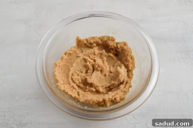 Keto cookie dough batter in a small glass mixing bowl on a white table after initial mixing, showing smooth texture.