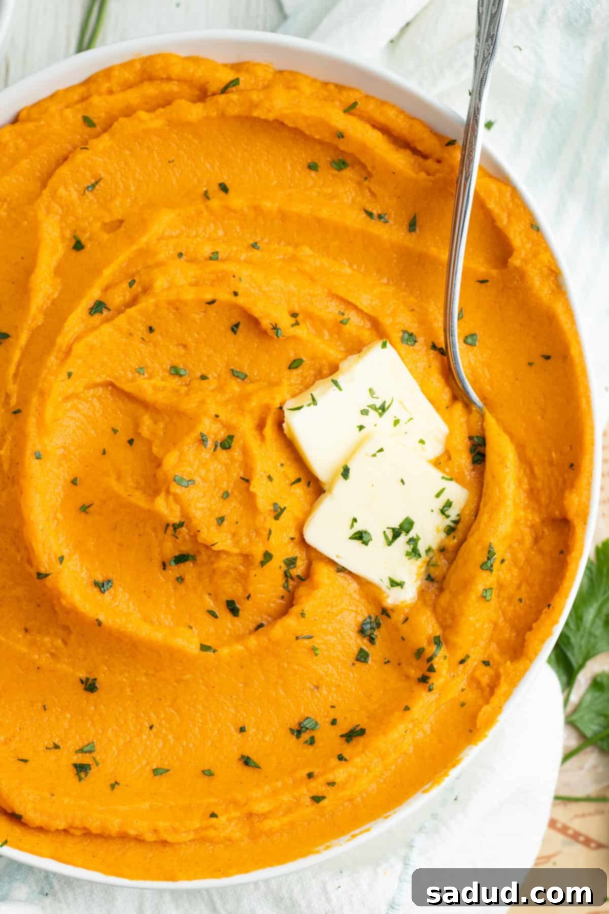 Overhead view of a bowl of whipped sweet potatoes with 2 pats of butter and fresh chives.