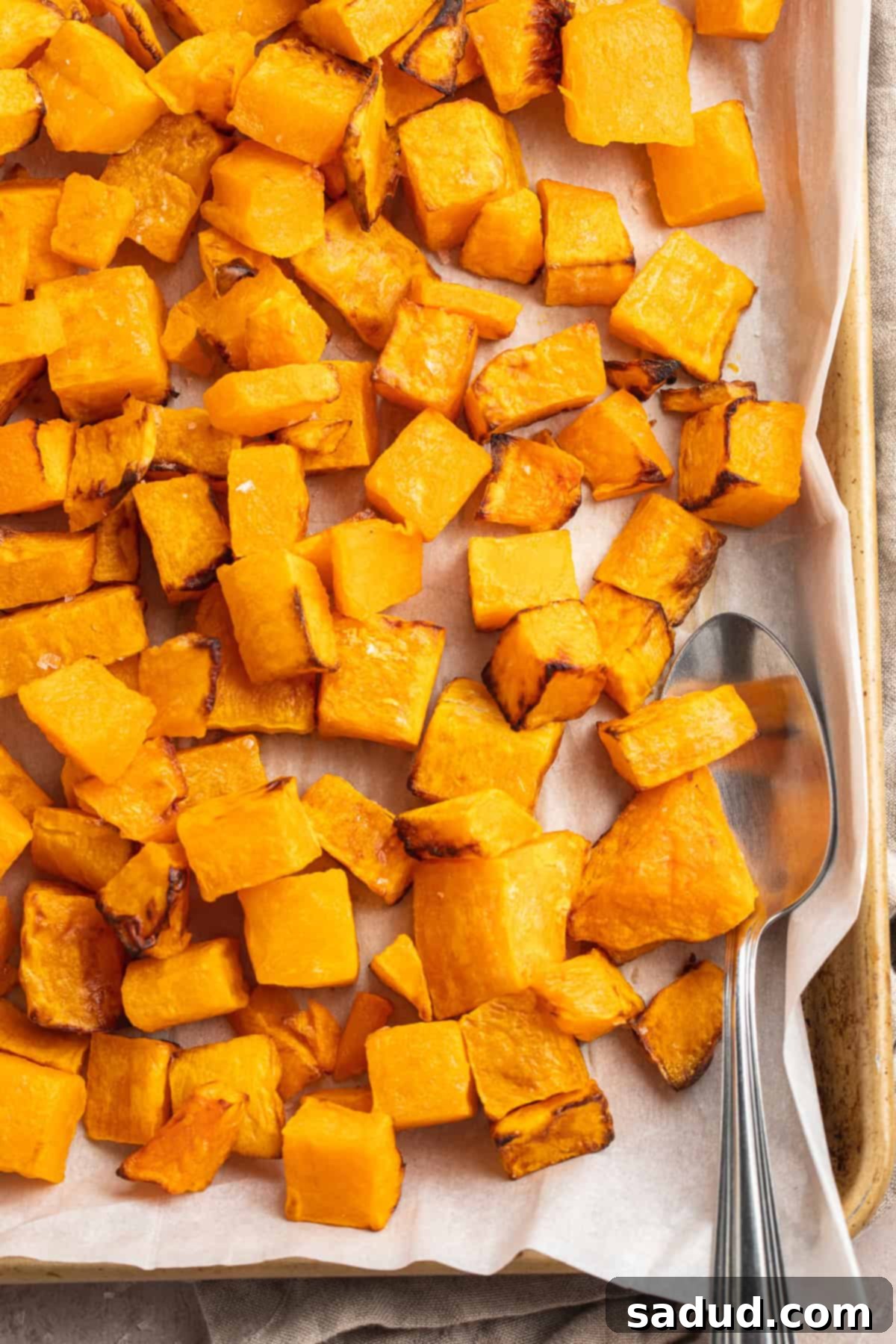 Overhead view of a sheet pan lined with parchment paper topped with cubed air fryer butternut squash, ready to be served.