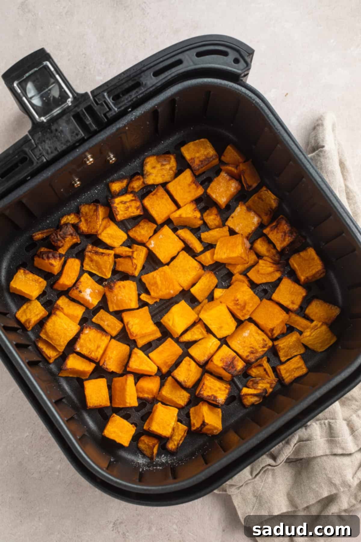 Overhead view of air fryer butternut squash in an air fryer basket, perfectly cooked and ready to be removed.