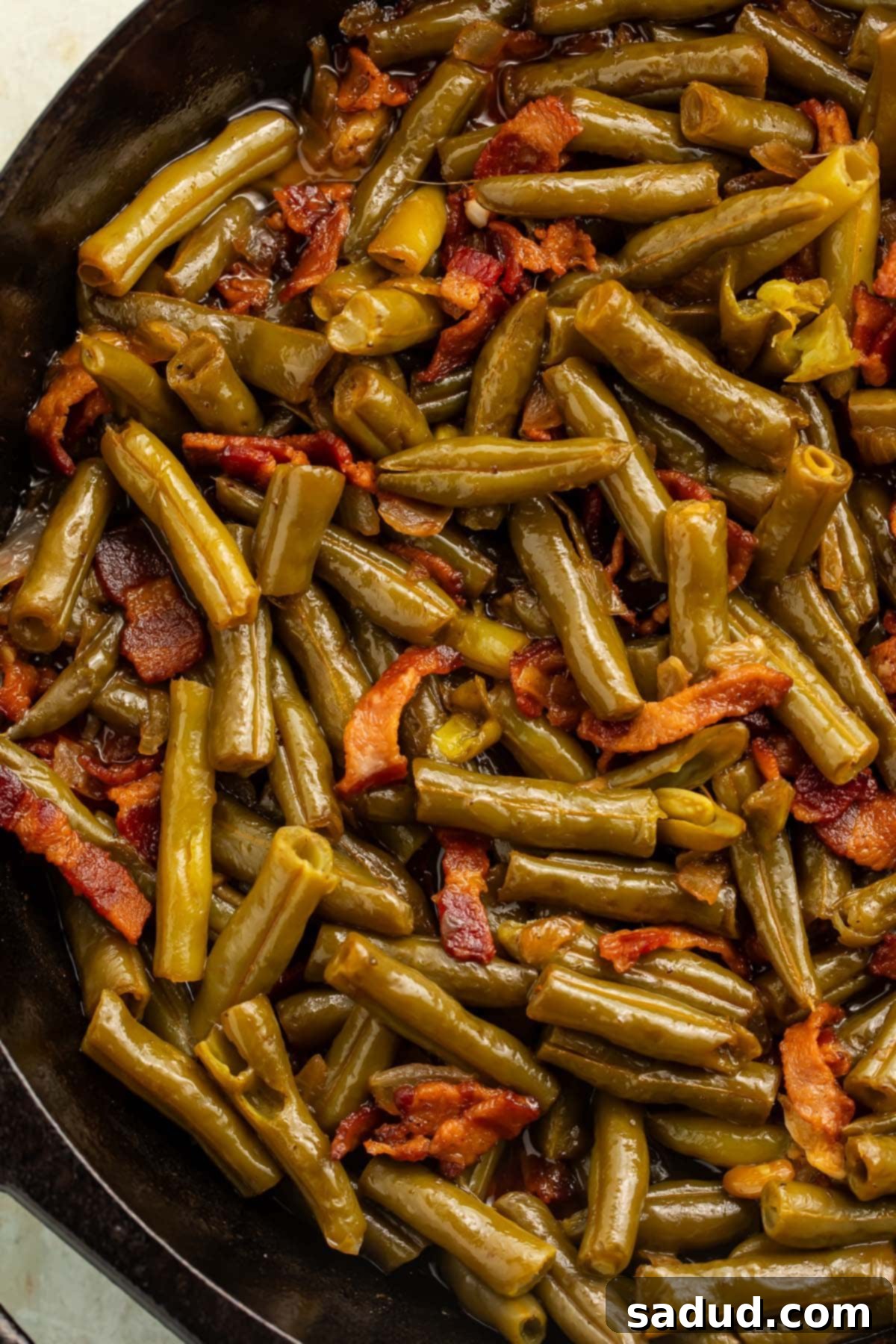 A large cast iron skillet brimming with vibrant Copycat Texas Roadhouse Green Beans, generously mixed with crispy bacon pieces and caramelized onions, ready to be served.