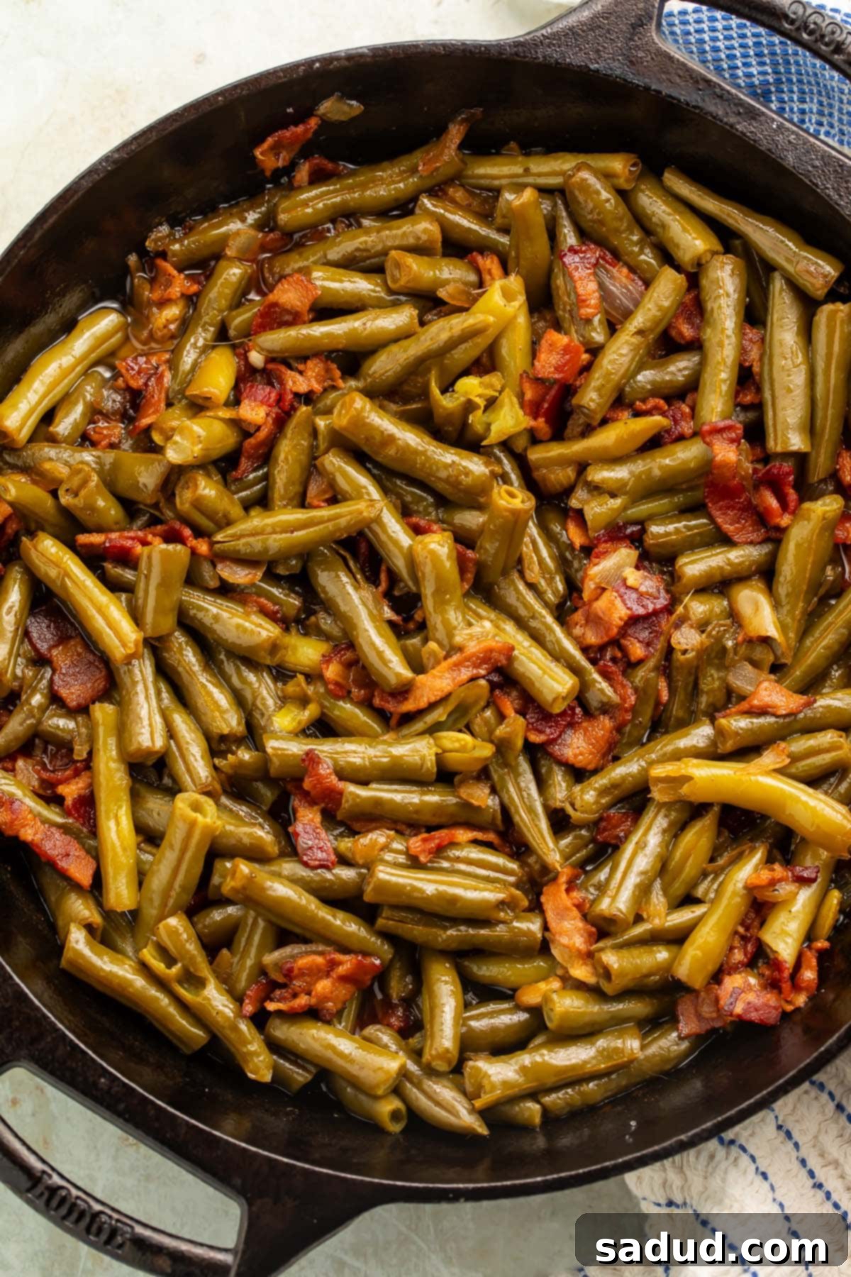 Close-up of savory Texas Roadhouse green beans, cooked with bacon and onions, served warm in a cast iron skillet.
