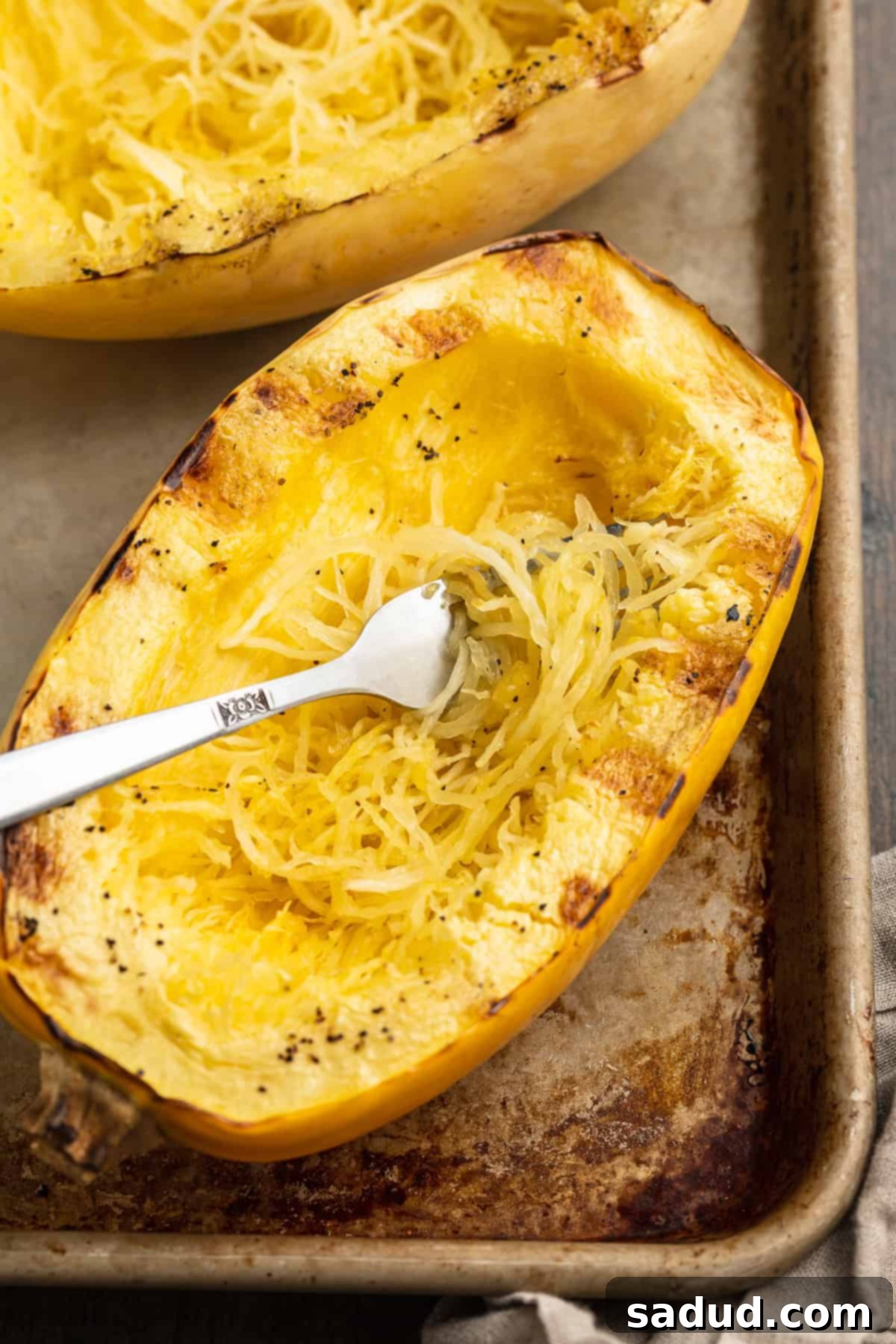Overhead view of a grilled spaghetti squash half on a baking sheet, showcasing its golden color and fibrous texture.