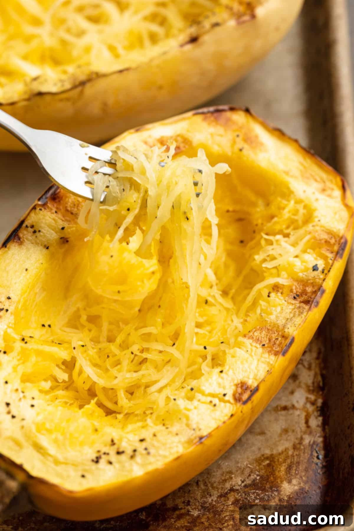 A fork lifting tender, stringy spaghetti squash out of a grilled half resting on a baking sheet, ready to serve.