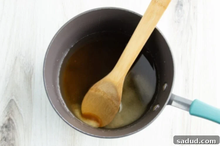 Overhead view of salt and brown sugar dissolved into a saucepan of boiling water, with a wooden spoon resting against the side of the pan, forming the brine base.