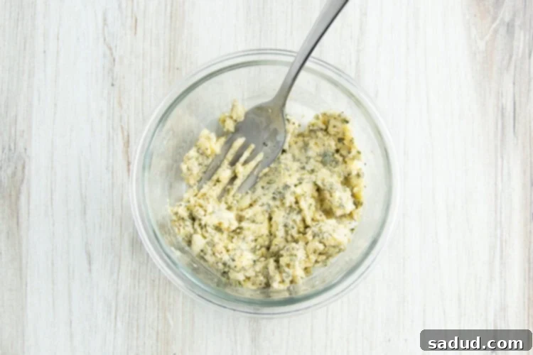 Overhead view of a small glass mixing bowl holding a mixture of butter, herbs, and seasonings with the fork used for mixing, ready to be applied to the turkey.