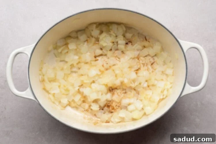 Overhead view of chopped onions and minced garlic gently sizzling in avocado oil in a large chili pot on a white table.