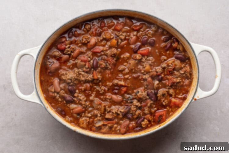 Overhead view of Mexican chili simmering in an oval chili pot on a white table, rich with tomatoes and beans.