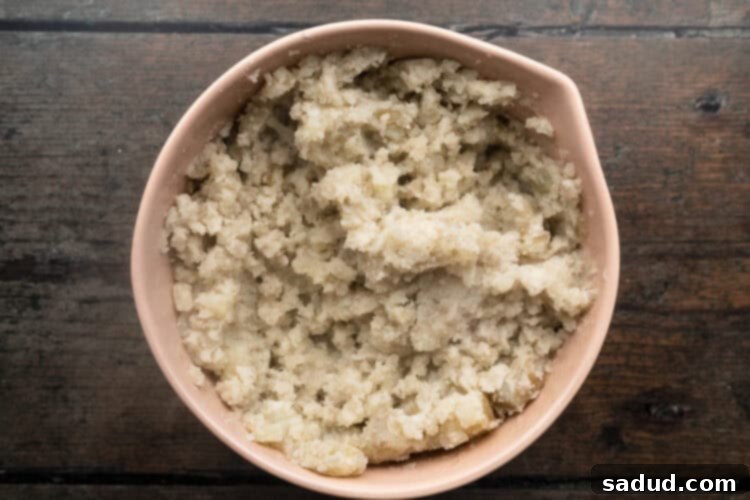 Overhead view of large beige mixing bowl holding roughly mashed potatoes, ready for the next steps.