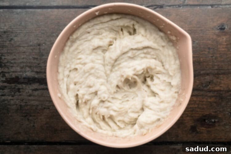 Overhead view of roughly mashed potatoes being mixed with hot milk until mixture is creamy and smooth.