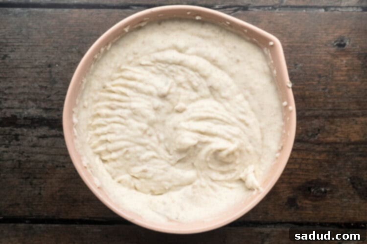 Overhead view of creamy whipped potatoes with milk, butter, and cream cheese in a large beige mixing bowl after whipping.