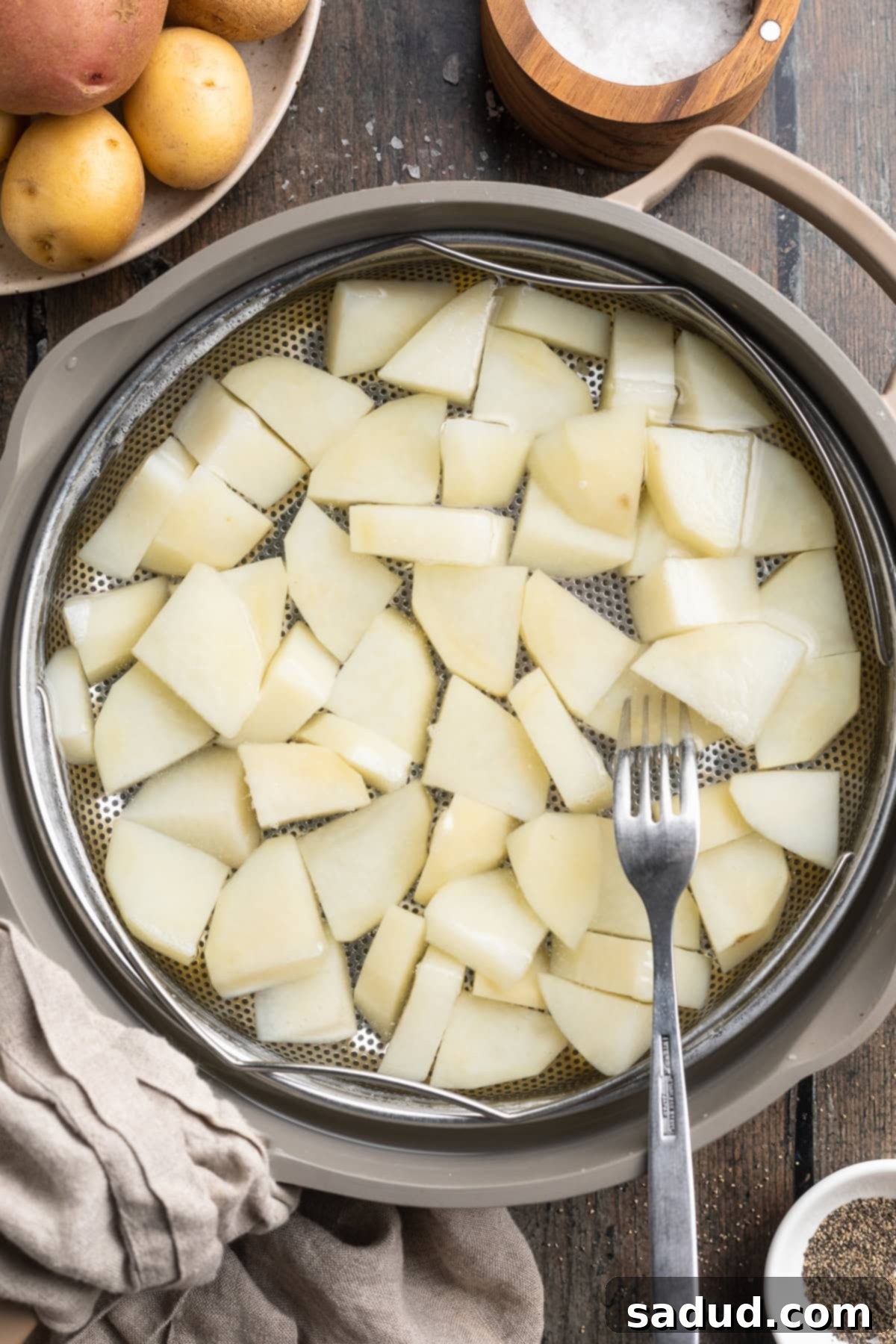 Overhead view of a silver pot of chopped, blanched potatoes on a table.