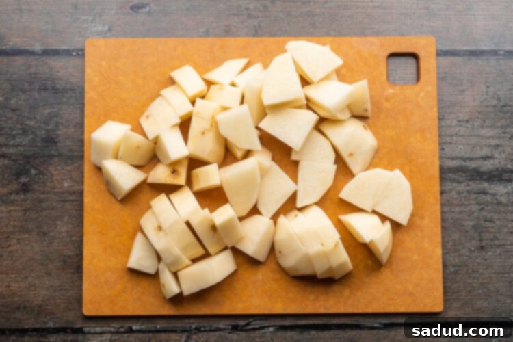 Overhead view of peeled, chopped potatoes on a wooden cutting board resting on a dark wooden tabletop.