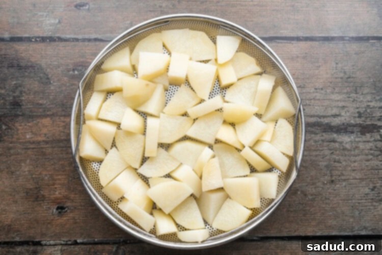 Overhead view of a bowl of cubed, blanched potatoes on a wooden tabletop.
