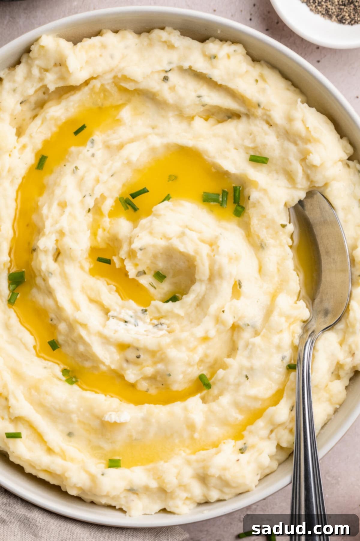 Overhead view of creamy Boursin mashed potatoes in a large bowl. Potatoes are garnished with chives and melted butter.