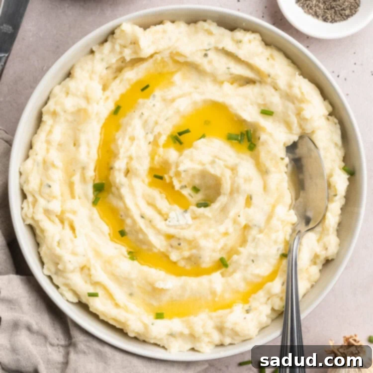 Overhead, zoomed out view of creamy boursin mashed potatoes in a large bowl. Potatoes are garnished with chives and melted butter.