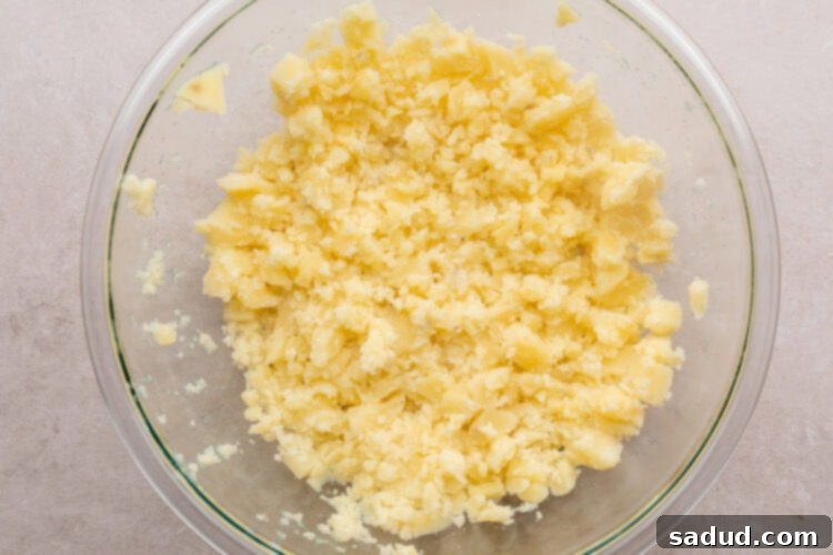 Overhead view of lightly mashed potatoes in a large glass mixing bowl on a neutral countertop.