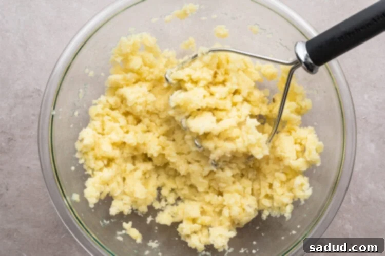 Overhead view of lightly mashed potatoes in a large glass mixing bowl on a neutral countertop.