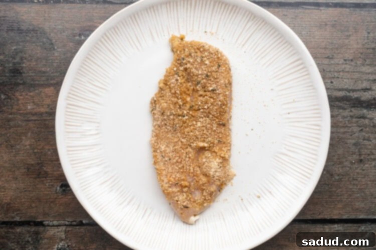 Breaded chicken cutlet resting on a large round white plate on a wooden table.