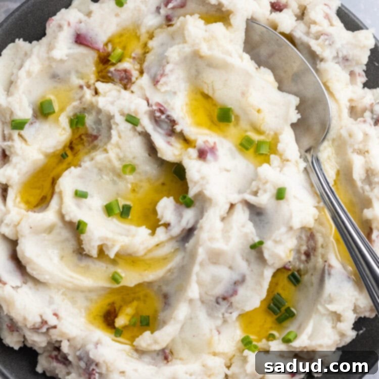 Fluffy, whipped, red skin mashed potatoes in a large blue-grey bowl with a spoon on a holiday table.