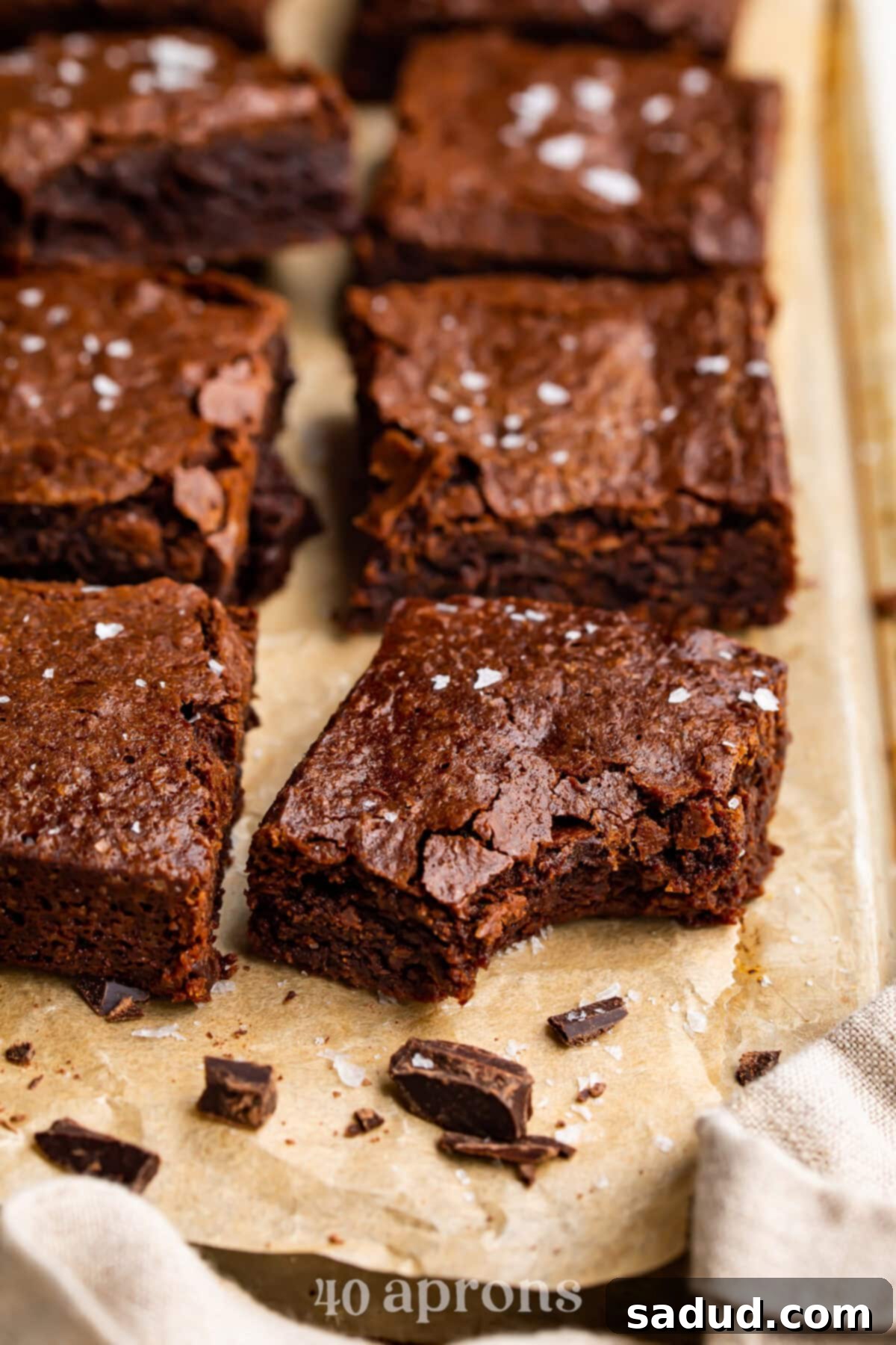 Decadent Dairy-Free Fudgy Brownies 3 A dairy-free brownie rests on a baking sheet covered in parchment paper. A bite is missing from the front corner of the brownie, revealing its rich, fudgy interior.