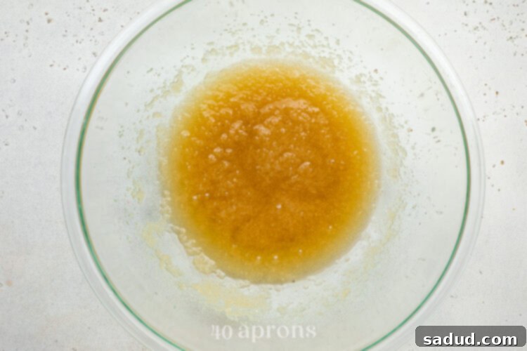 Wet ingredients for dairy-free brownies in a large glass mixing bowl: melted coconut oil, sugar, and vanilla extract.