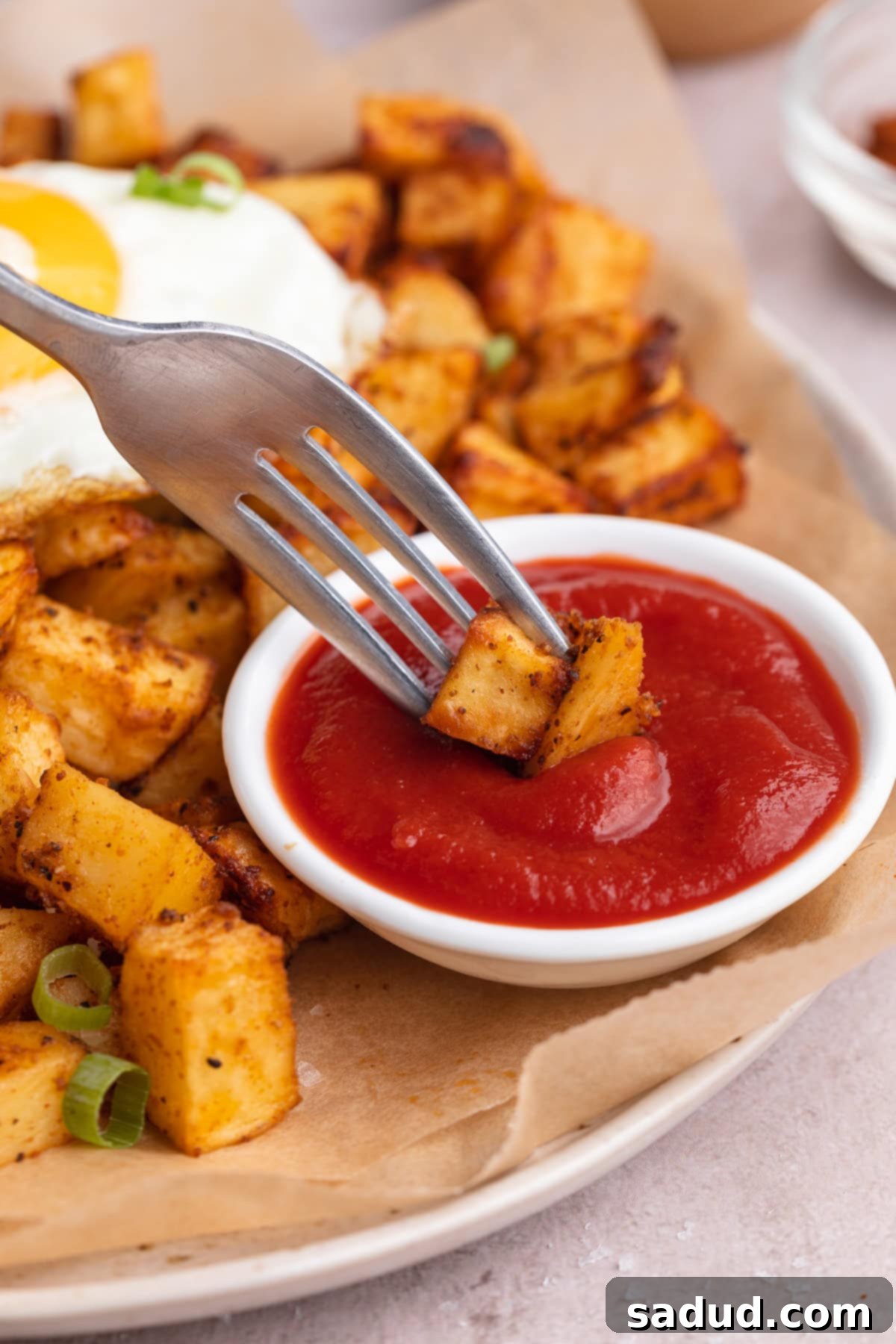 Crispy Air-Fried Morning Spuds 3 Air fryer breakfast potatoes on the end of a fork, being dipped into a small ramekin of ketchup.