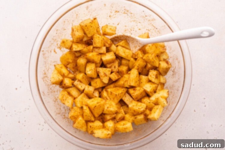 Overhead bowl with cubed potatoes, neutral oil, and several spices.