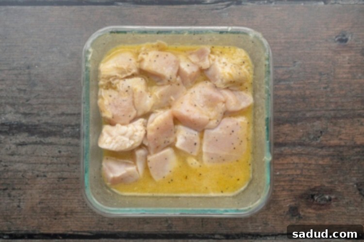 Chunks of chicken breasts marinating in a square glass pan filled with lemon juice and white wine.