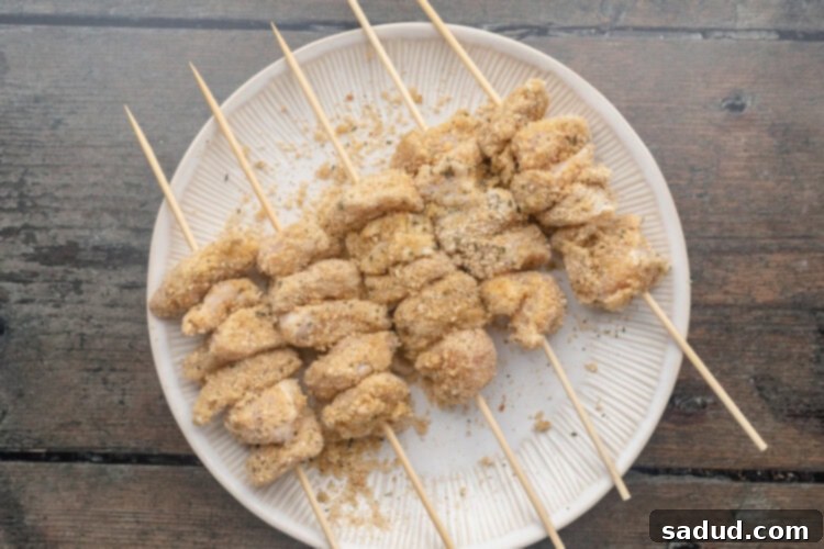 Skewered and breaded chicken chunks resting on a round white plate.