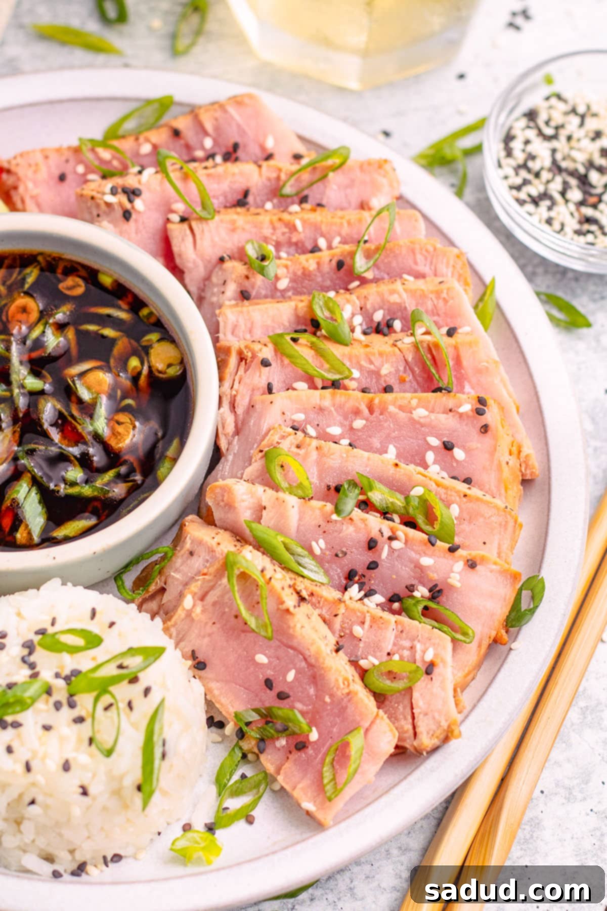 Garnished air fryer tuna steaks, arranged artfully around a small bowl of soy dipping sauce, accompanied by a side of fluffy white rice and sliced green onions.
