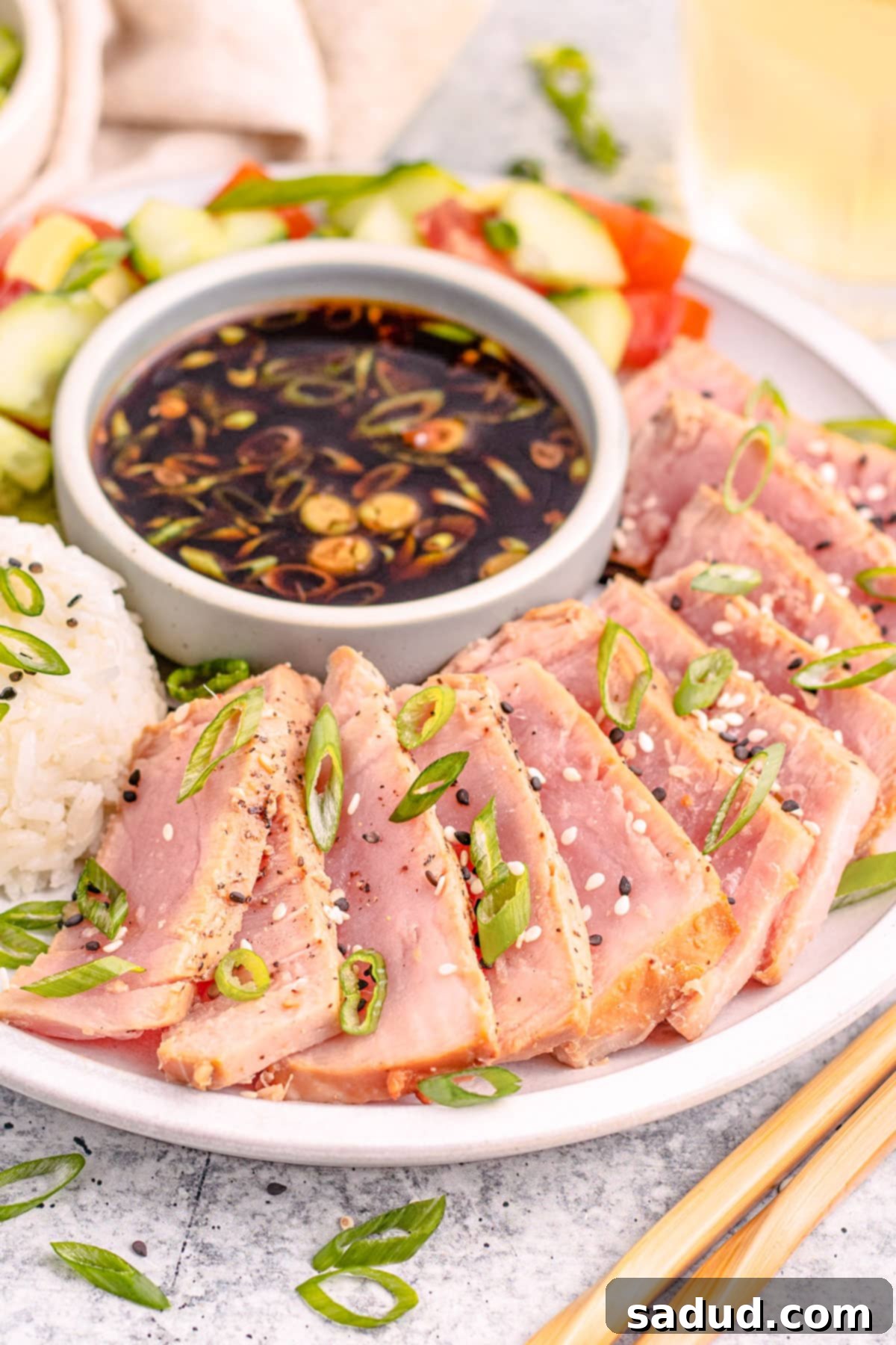 Air fried tuna steaks, thinly sliced and garnished with green onions and sesame seeds, resting on a bed of white rice with a side of dipping sauce.